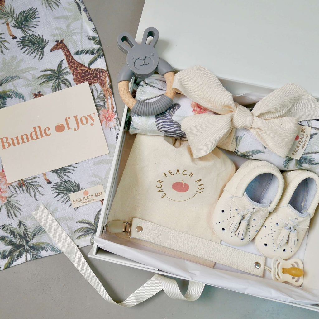 Luxury baby gift box set in ivory with Filly soft sole baby shoes in ivory, organic leather dummy clip in ivory, BIBS Supreme dummy in ivory, BPA-free teether and organic cotton muslin baby swaddle in jungle safari print